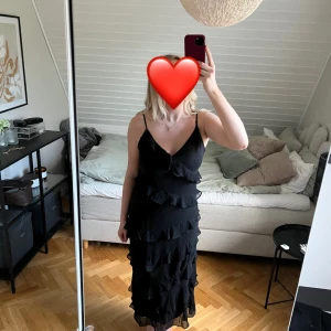 Svart klänning med volanger - Snygg svart klänning med volanger och smala axelband. Perfekt för en elegant look med en touch av lekfullhet. Endast använd en gång och inga defekter! 