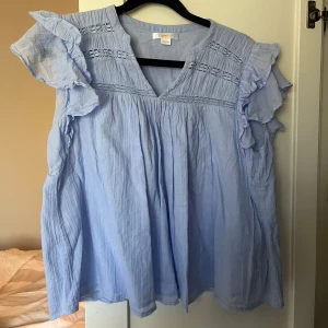 Ljusblå blus med volangdetaljer - Säljer en söt ljusblå blus med volangdetaljer på ärmarna och v-ringning