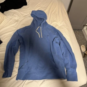 Blå hoodie från Ralph Lauren - Säljer en snygg blå hoodie från Ralph Lauren med en liten broderad logga på bröstet. Tröjan har en klassisk känguruficka och justerbar huva med snören. Perfekt för en avslappnad stil.