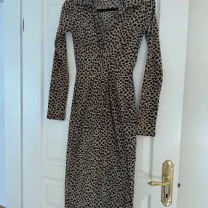 Leopardmönstrad långärmad klänning - Säljer en snygg långärmad klänning med leopardmönster i beige och svart. Klänningen har v-ringning och markerad midja för en smickrande passform. Perfekt för dig som vill sticka ut med ett djurmönstrat plagg.