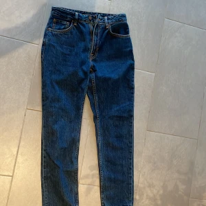 Blå jeans från Nudie Jeans - Säljer ett par klassiska blå jeans från Nudie Jeans med raka ben och normal passform. Jeansen har fem fickor, orange sömmar och Nudie-logga på bakfickan. Perfekta för dig som gillar tidlös denimstil.  Säljer dem för 350kr