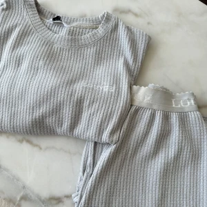 Grå ribbad lounge-set från Lounge - Mysigt grått lounge-set från Lounge med ribbad textur. Toppen har trekvartsärmar och en avslappnad passform. Byxorna har en elastisk midja med logotypdetalj. Perfekt för en avslappnad dag hemma.