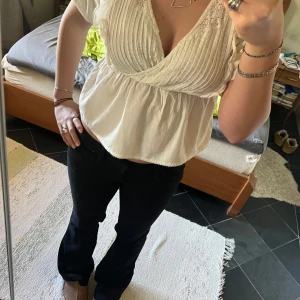 Vit blus med spetsdetaljer - Säljer en söt vit blus med spetsdetaljer, volang och v-ringning. Blusen har korta ärmar och en omlott-design framtill. Perfekt för en avslappnad men stilren look. Använd enstaka gång 💓