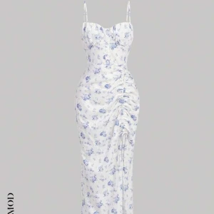 Vit blommig långklänning med smala axelband - Elegant vit långklänning med blått blommönster och smala axelband. Klänningen har en åtsittande passform. Perfekt för en härlig sommar dag på stranden. Köptes för 129kr