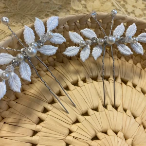 Hårnålar med vita blad och pärlor - Två eleganta hårnålar dekorerade med vita blad i plast och skimrande pärlor samt små glittriga stenar. Perfekt accessoar för att ge håret en romantisk och unik touch. Bladen har en detaljerad struktur och pärlorna ger en lyxig känsla. Finns fler kvar, samma frakt 