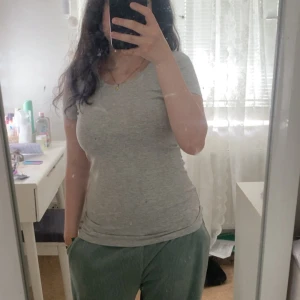 Grå basic t-shirt med rund hals - Enkel och stilren grå t-shirt med rund halsringning och korta ärmar. Modellen är figurnära och passar perfekt till jeans eller mjukisbyxor. Gjord i mjuk bomull som känns skön mot huden. Perfekt för dig som gillar en clean och avslappnad look.