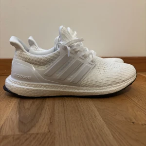 Vita Adidas Ultraboost - Fräscha helvita Adidas Ultraboost sneakers med stickad ovandel och klassiska tre ränder på sidorna. Skorna har snörning, platt sula och en riktigt bekväm Boost-mellansula. Perfekta för dig som gillar stilrena och sportiga vibes. Skorna är i nyskick tveka inte över att höra av dig vid frågor😁