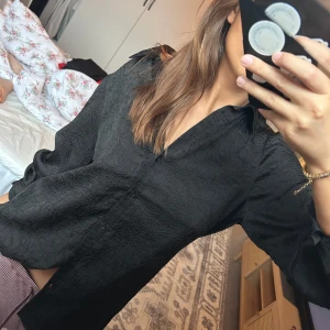 Svart skjorta med struktur och knappar - Säljer en svart skjorta med snyggt strukturerat tyg och klassisk krage. Skjortan har lång ärm och knäppning framtill. Passformen är normal och materialet känns lätt och luftigt, perfekt för att lyfta vilken outfit som helst.