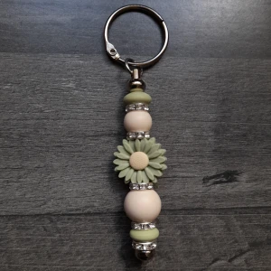 Nyckelring handgjord med silikonpärlor  - Handgjord nyckelring med gröna och beige pärlor samt en söt blomma i mitten. Dekorativa silverdetaljer ger extra bling. Perfekt accessoar för att piffa upp dina nycklar eller väska.