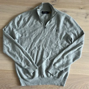 Grå half zip tröja Polo Ralph Lauren - Snygg grå tröja från Polo Ralph Lauren med half zip och diskret broderad logga på bröstet. Tröjan är långärmad och har ribbade muddar och krage. Perfekt för lager-på-lager och chill stil. Gjord i mjuk bomull för skön känsla.