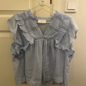 Ljusblå volangblus från Neo Noir - Ljusblå blus från Neo Noir med volanger längs axlarna och v-ringning. Blusen är ärmlös och har fina broderade detaljer samt en luftig, flowy passform. Passar s-l storlek. I utmärkt skick!🥰