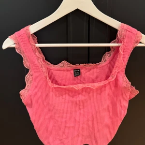 Rosa ribbad linnetopp med spets - Supersöt rosa linnetopp från SHEIN med ribbad struktur och breda axelband dekorerade med spets. Toppen har fyrkantig ringning och är perfekt för dig som gillar en feminin och trendig look.