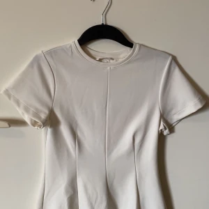 Vit topp från H&M med sömdetalj - Säljer en stilren vit topp från H&M i storlek S. Men skulle säga att tröjan även passar M, då den är lite förstor på mig som vanligtvis har Xs-S. T-shirten har korta ärmar, rund halsringning och en snygg söm mitt fram som ger en clean look. Perfekt att matcha med jeans eller kjol för en enkel men fräsch outfit.