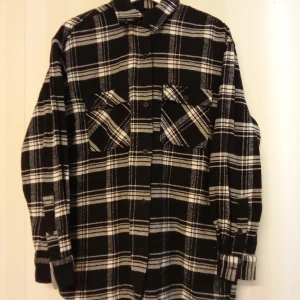 Svartvit rutig overshirt från Bik Bok - Overshirt i svart och vitt från Bik Bok med rutigt mönster, tillverkad i 100% bomull. Skjortan har klassisk krage, knäppning framtill och två stora bröstfickor. Perfekt att slänga över en hoodie eller t-shirt för en chill look. Kan skickas med extra pris via post.