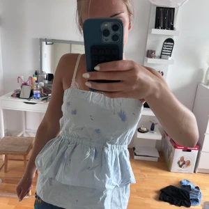 Ljusblå volangig tubtopp med mönster - Supersöt ljusblå tubtopp med volang och tunna axelband. Toppen har ett diskret blått mönster med små fjäderliknande detaljer och resår i midjan för en snygg passform. Perfekt till jeansshorts eller kjol för en chill sommarlook.