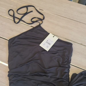 Svart klänning BikBok XS - Supersnygg svart klänning från BikBok i slimmad modell med smala axelband som knyts i nacken. Klänningen har rynkade sidor. Aldrig använd, lappar hänger kvar.