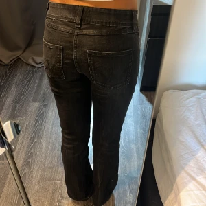 Svarta bootcut jeans med dubbla knappar - Säljer ett par svarta jeans med bootcut-modell och snygg tvätt. Byxorna har dubbla knappar i midjan, klassiska fickor fram och bak samt bälteshällor. Perfekta för dig som gillar en tidlös look med lite edge.