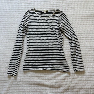 Randig långärmad topp från H&M - Snygg långärmad topp från H&M i svartvitt randigt mönster. Tröjan har rund halsringning och är gjord i mjuk bomull, perfekt för en chill och stilren look. Passformen är normal och materialet är tunt och skönt mot huden.