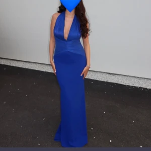 Kornblå långklänning med djup v-ringning - Snygg kornblå långklänning med djup v-ringning och figurnära passform. Klänningen är ärmlös och har breda axelband som ger en elegant siluett. Perfekt för bal eller festliga tillfällen. Passar en 36-40