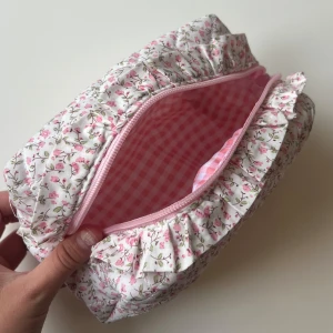 Quiltad blommig necessär med volang - Supergullig quiltad necessär i vitt med små rosa blommor och volangdetaljer runt dragkedjan. Insidan är fodrad med rosa och vitt rutigt tyg. Perfekt för smink eller småprylar, stängs med ljusrosa dragkedja. Mjuk och fluffig känsla. Superfin 