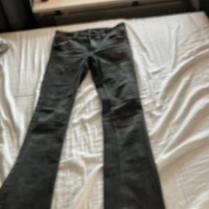 Svarta bootcut jeans från H&M - Säljer ett par svarta bootcut jeans från H&M med låg midja och justerbar midja. Jeansen har snygga fickdetaljer med knapp och klassisk tvättad look. Perfekta för dig som gillar en retro vibe och vill ha en bekväm passform.