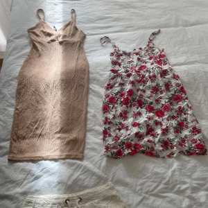 Beige ribbad klänning & blommig klänning - Två klänningar: en tight, ribbad beige kortklänning med smala axelband och en vit kortklänning med röda blommor och smala axelband. Perfekta för sommaren och ger en fräsch och trendig look.