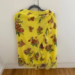 Gul blommig omlottkjol med volang - Superfin gul omlottkjol med blommigt mönster och volangdetaljer. Kjolen är luftig och perfekt för varma dagar, med en härlig sommarkänsla och snygg passform. Kan mötas upp i Trollhättan eller Alingsås. Kan skickas men då tillkommer en fraktkostnad.
