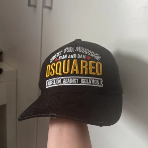 Svart keps från Dsquared2 med brodyr - Svart keps från Dsquared2 med broderad text i gult och vitt framtill och baktill. Justerbar rem baktill för perfekt passform. Klassisk böjd skärm och coola detaljer som 'Fight for Freedom' och 'Killers on the Loose'. Materialet är bomull.