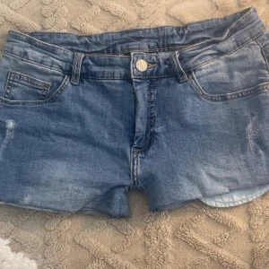 Lågmidjade jeansshorts med slitningar - Snygga blå jeansshorts med klassisk femficksdesign och lätt slitna detaljer. Shortsen har normal passform, uppvikta benslut och dragkedja med knapp framtill. 💕 de är också lågmidajde. 👏 vill bli av med så jag ge emot vissa prisförslag! 💕 storlek 38, men de är omsydda så de passar nog 34-36! 