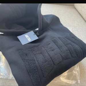 Svart hoodie från Aretha med brodyrHelt ny i förpackning strl small Luv tröja med snygg lurviga logga Aretha 44cm bredd axelLängd ca 70 cm (Har en i medium också i en annan annons) - Svart hoodie från Aretha i 100% bomull med stor broderad text framtill. Klassisk huva och mjuk insida, perfekt för en chill och stilren look. Snyggt minimalistisk design med diskret branding och relaxed passform.Helt ny i förpackning strl small   Luv tröja med snygg lurviga logga Aretha 44cm bredd axel Längd ca 70 cm   (Har en i medium också i en annan annons)