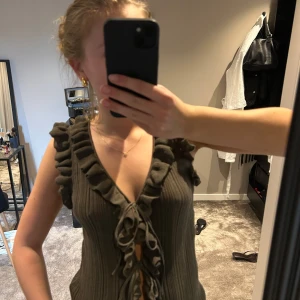 Olivgrön topp med volang - Supersnygg olivgrön ribbad topp med djup v-ringning, volangkant längs urringningen och knyt framtill. Ärmlös modell som ger en cool och trendig vibe. Från Zara och lappen har jag tyvärr klippt bort men den passar mig som vanligtvis har S/M i toppar!! Använd 1 gång