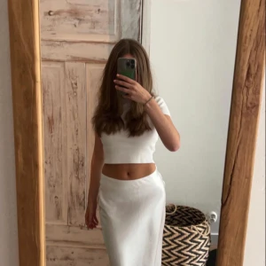 Vit långkjol i satin - Säljer en stilren vit långkjol i glansigt satinmaterial. Kjolen har en rak och flowy passform som sitter snyggt i midjan och faller mjukt ner mot anklarna. Perfekt för dig som gillar minimalistisk och clean stil.