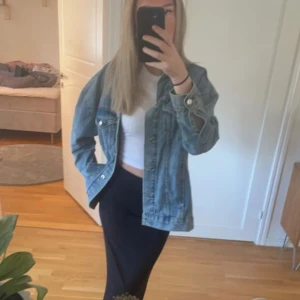 Oversized jeansjacka i ljusblå denim - Säljer en oversized jeansjacka i ljusblå denim med klassisk krage, bröstfickor med knappar och långa ärmar. Jackan har en avslappnad passform och silverfärgade knappar framtill. Perfekt att slänga över en hoodie eller crop top för en chill look.