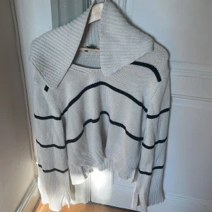 Randig stickad tröja från Lindex - Säljer en beige stickad tröja från Lindex med svarta ränder och stor krage. Tröjan har lång ärm, ribbade muddar och en lite loose passform. Perfekt för dig som gillar en chill och trendig look.