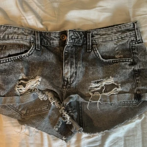 Grå slitna jeansshorts från H&M - Säljer ett par grå jeansshorts från H&M med slitna detaljer och fransig kant. Shortsen har klassisk femficksmodell, låg midja 