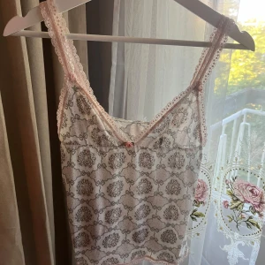 Söt spets linnetopp med rosett - Söt linnetopp i rosa/vitt med grått mönster och spetskant i ljusrosa. Står ej storlek eller märke men är som XS/S