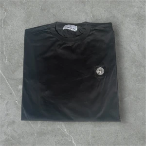 Svart t-shirt från Stone Island - Säljer en svart t-shirt från Stone Island med rund hals och liten broderad logotyp på bröstet. Enkel och stilren design som passar perfekt till jeans eller shorts.