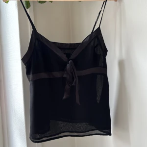 Svart linnetopp  - Säljer en svart linnetopp från Å med tunna axelband och knytning framtill. Toppen har en lätt och luftig känsla. Dragkedja i sidan för enkel på- och avtagning. Perfekt för fest och vardag. Köpt second hand men själv aldrig andvänt då den inte passade. 