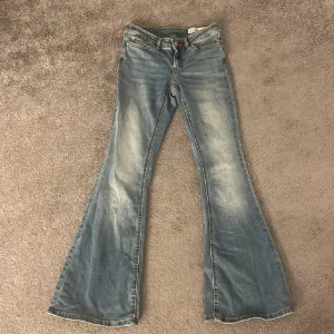 Blå bootcut jeans - Säljer ett par blå low waist bootcut jeans med lätt slitning framtill och bak. Jeansen har normal passform och stängs med dragkedja och knapp. I storlek xs från veromoda. 