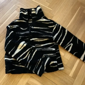 Svart och vit fleecejacka med zebramönster - Mysig fleecejacka i svart med vit zebramönster. Jackan har hög krage och dragkedja framtill. Perfekt för kyliga dagar när du vill ha något både snyggt och bekvämt. ⚠️jackan är vitt det är ljuset som gör den lite gul aktig.pris kan diskuteras.
