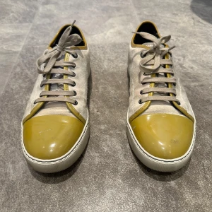 Lanvin - Säljer ett par beige sneakers från Lanvin med unika guldfärgade, lackade tår och vita snören. Skorna har rund tå och platt sula, samt diskreta metallöglor för snörningen. Perfekta för dig som vill sticka ut med en cool detalj. Storlek 42/43 men skulle personligen säga att dom är lite stora i storleken. Hörgärna av er vid frågor och pris kan diskuteras vid snabb affär.