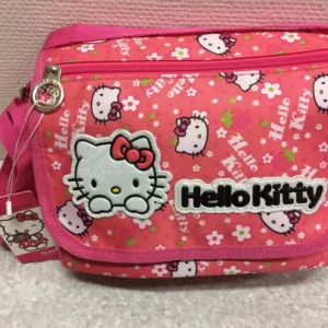 Rosa Hello Kitty axelväska - Supergullig rosa axelväska med Hello Kitty-motiv och blommor. Väskan har ett stort Hello Kitty-tryck framtill, dragkedja och justerbar axelrem. Perfekt för dig som älskar söta accessoarer! Mått 25.00*21.00*10.00 cm 