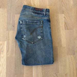 Blå Dondup George jeans med slitningar - Säljer ett par sjukt feta dondup blå jeans med flera trasiga och slitna detaljer fram och baktill. Jeansen har normal passform och klassisk femficksdesign. De är tillverkade i denim och har en rak siluett med låg midja. Perfekta för en avslappnad och trendig look. W33 men passar antagligen dig som har lite mindre också Hör av er vid frågor! Obs priset ej hugget i sten!