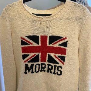 Beige stickad tröja med Union Jack från Morris - Säljer en jättefin men välanvänd tröja från Morris. Den är i fint skick och har inga defekter! Säljer för att jag inte har så stor användning av den längre 🥰😊