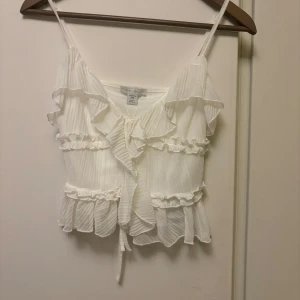 Vit volangprydd linnetopp från Ivyrevel - Supersöt vit linnetopp med tunna axelband och volangdetaljer framtill och längs kanterna. Toppen har knyt framtill, aldrig använd💕