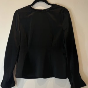 Svart långärmad blus från Gina Tricot - Säljer en stilren svart blus från Gina Tricot i storlek 38. Blusen har långa ärmar och rund halsringning, samt en diskret dragkedja i nacken. Perfekt för en enkel och elegant look.