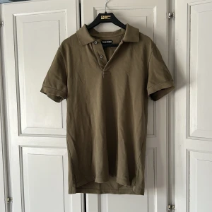 Olivgrön pikétröja från Tom Ford - Säljer en stilren olivgrön pikétröja från Tom Ford. Tröjan har klassisk krage, korta ärmar och knäppning framtill. Perfekt för en avslappnad men snygg look. Materialet är mjuk bomull som känns skönt mot huden. I princip oanvänd. 