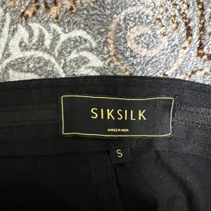 Svarta cargobyxor från SikSilk - Svarta cargobyxor från SikSilk med flera fickor på sidorna och avslappnad passform. Byxorna har elastiska benslut och klassisk cargostil, perfekta för en streetwear-look.