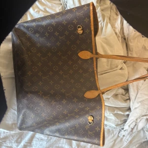 Louis Vuitton Neverfull Monogram axelväska - Säljer en klassisk Louis Vuitton Neverfull i storlek GM. Den är som ni ser på bilderna väl använd men fortfarande fin. Läderbanden på sidorna har tidigare gått sönder vilket gjorde att jag klippte av dem. Banden är som ni ser även sköra och dom kommer behöva bytas ut i framtiden. Jag har använt den i detta skicket med en del packning i ca 2 månader utan att den gått sönder, den är alltså fortfarande i användbart skick. Canvasen är i fint skick,inga repor. Kom dm för mer info🤗