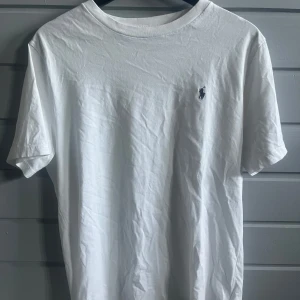 Vit t-shirt från Ralph Lauren - Klassisk vit t-shirt från Ralph Lauren med liten broderad logga på bröstet. Enkel och stilren design med rund hals och korta ärmar. Perfekt basplagg för garderoben. Pris kan diskuteras.